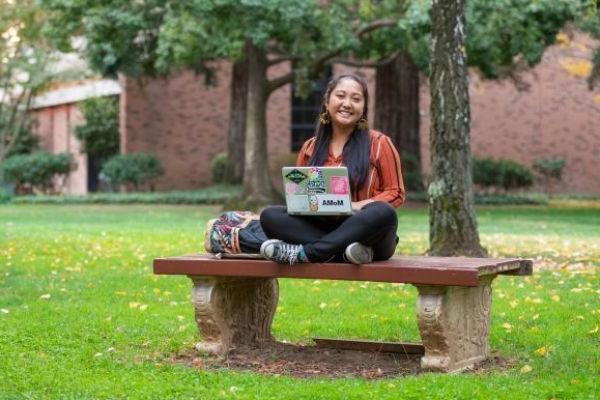 a student sits on a bench with a laptop